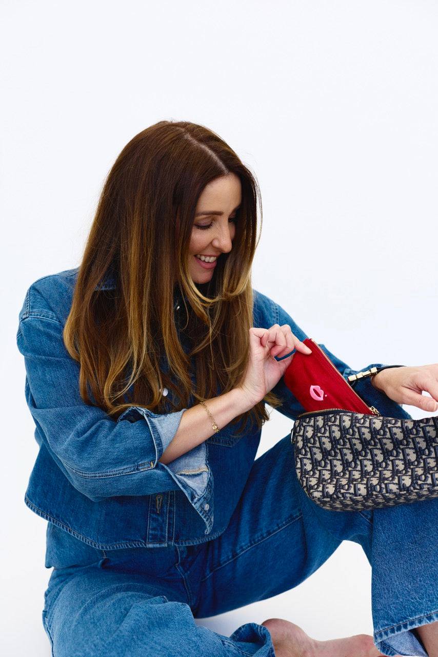 Woman placing cherry red Pout Pouch velvet makeup pouch into handbag