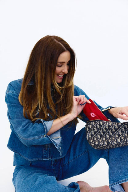 Woman placing cherry red Pout Pouch velvet makeup pouch into handbag